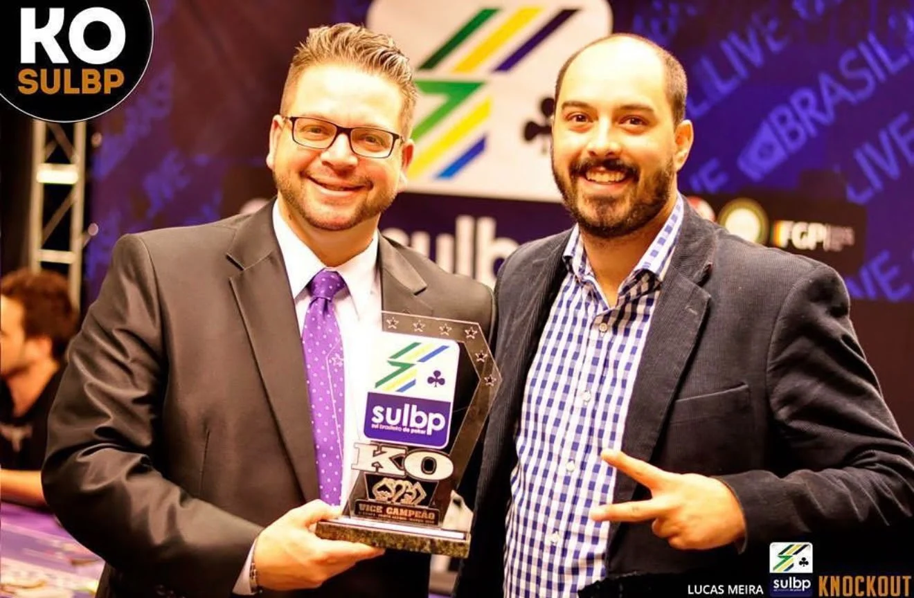 Lucas Meira em evento de poker, recebendo reconhecimento ao lado de outro participante